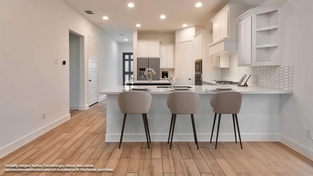 Wood-finish flooring, recessed lighting, white shaker cabinetry, tiled backsplash, and stainless steel appliances