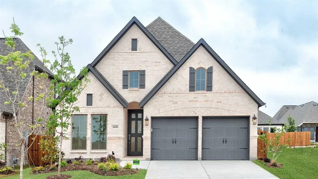 Light-colored brick exterior with dark trim accents, featuring a prominent gable roofline and a two-car garage with carriage-style doors