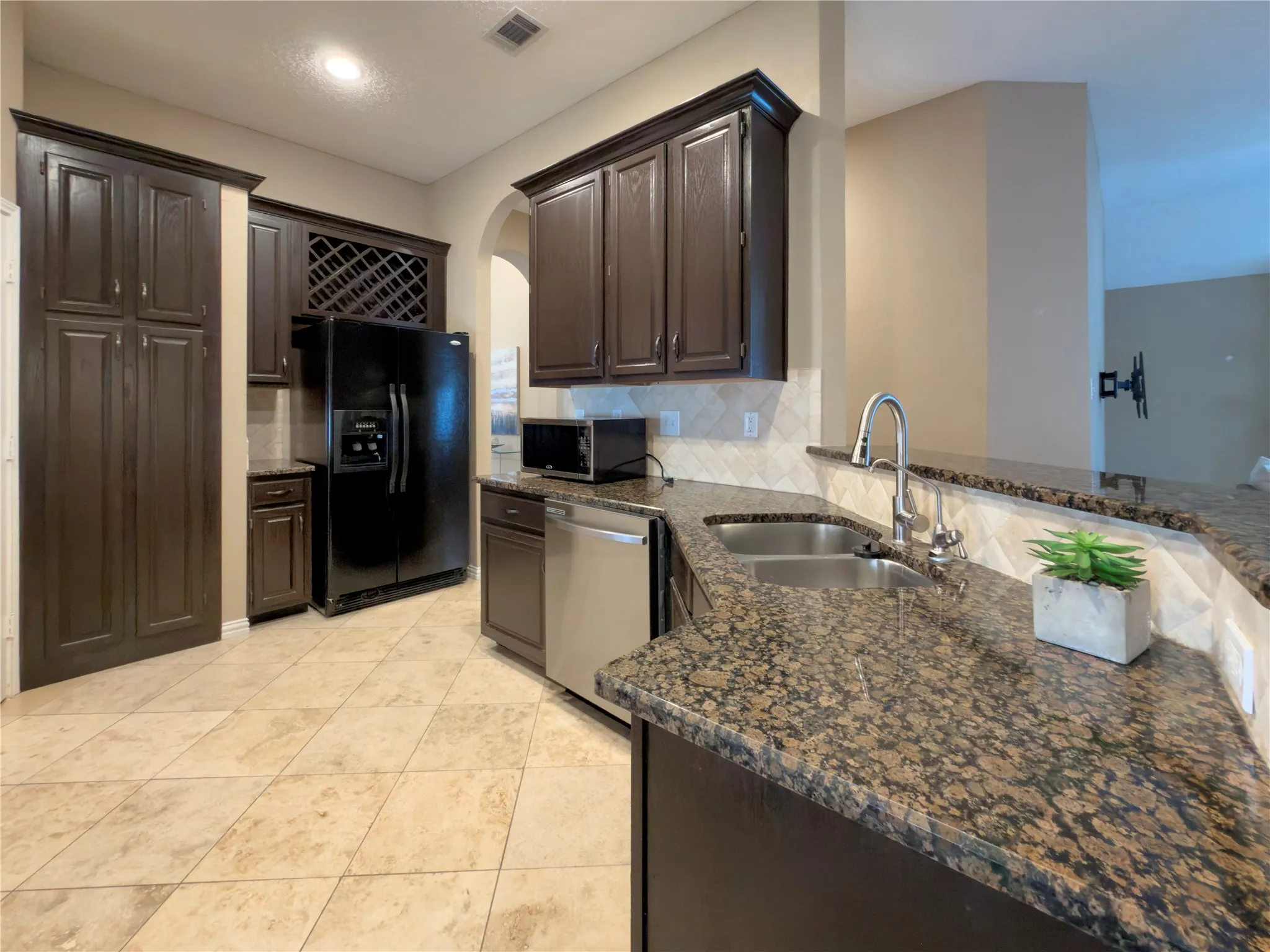 Kitchen featuring dark wood cabinetry, granite countertops, tile backsplash, and stainless steel appliances