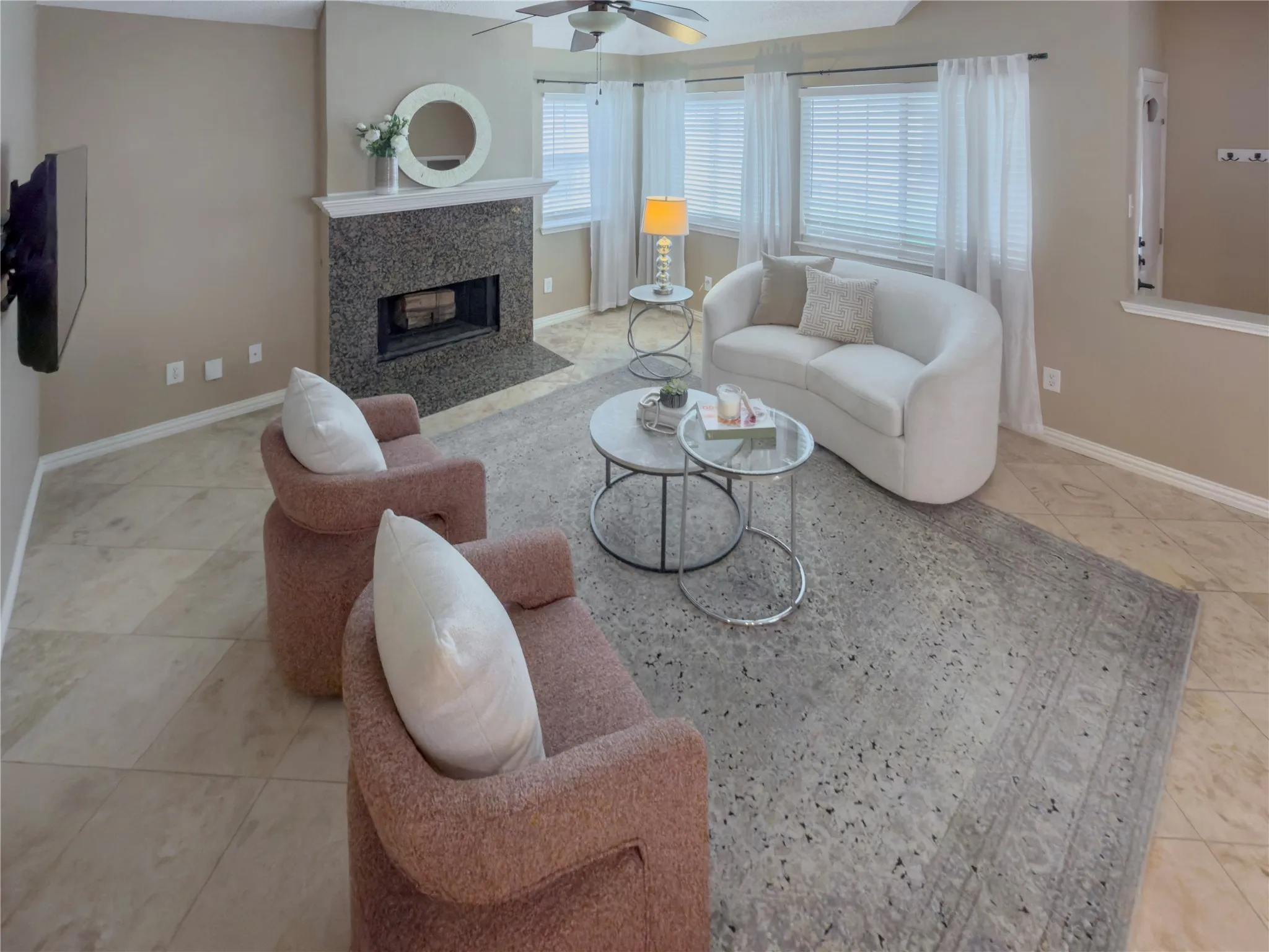 Tile flooring with a fireplace featuring a stone surround and hearth, multiple windows, and a ceiling fan