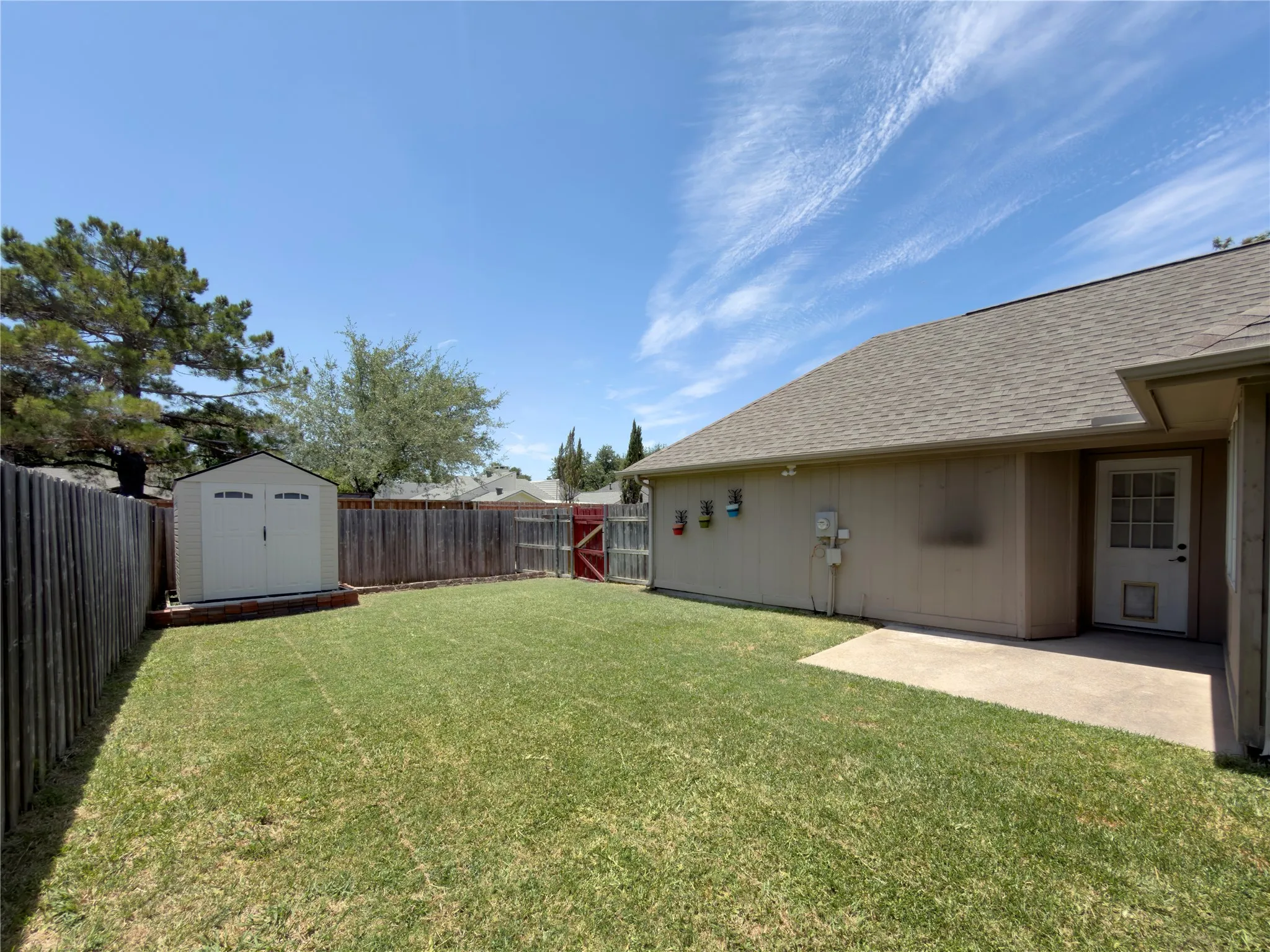 Expansive fenced backyard featuring a grassy lawn, a storage shed, and an exterior door with paneling