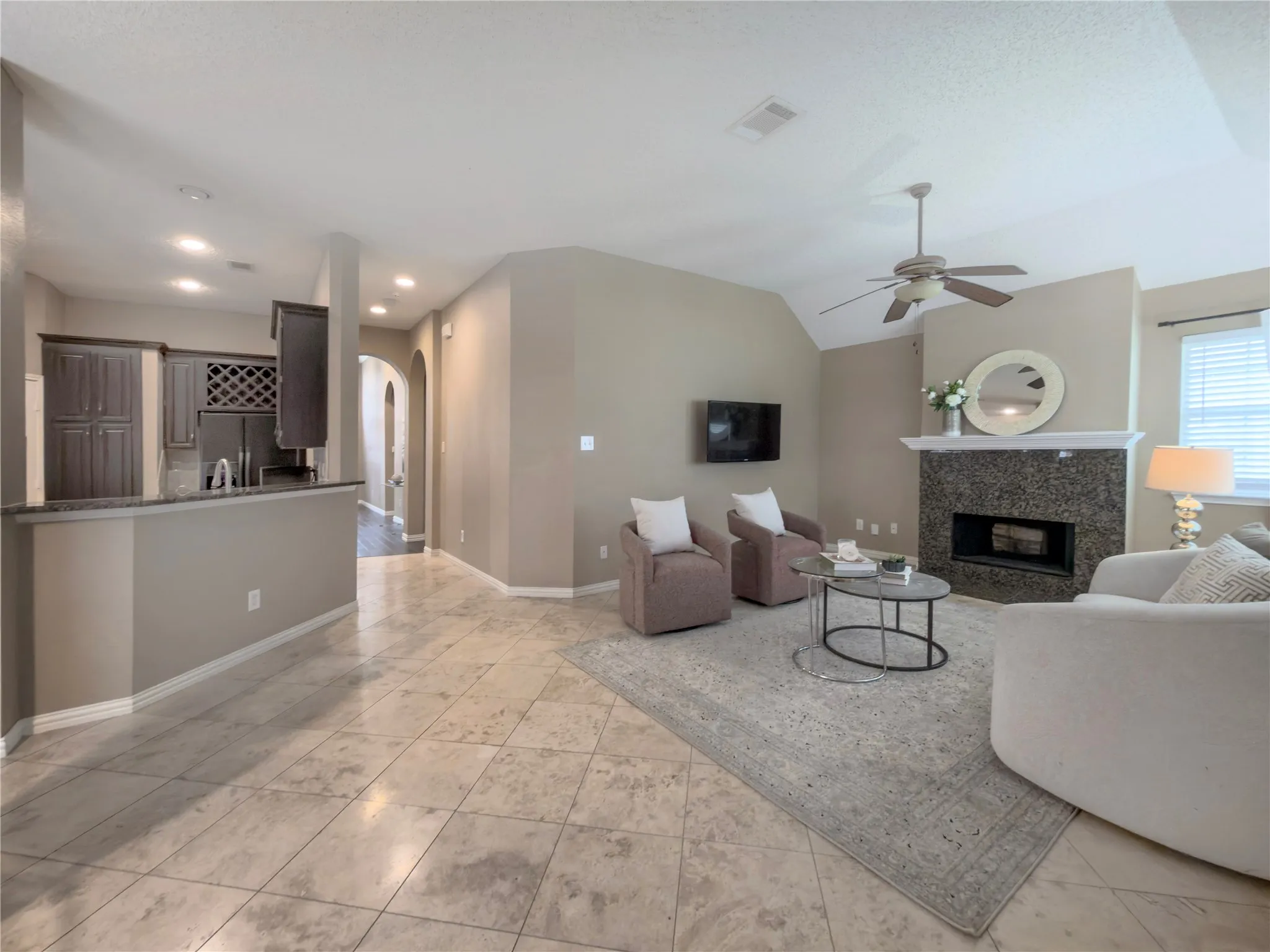 Living area with tiled flooring, fireplace with stone surround, vaulted ceiling with fan, and a kitchen bar with built-in cabinetry