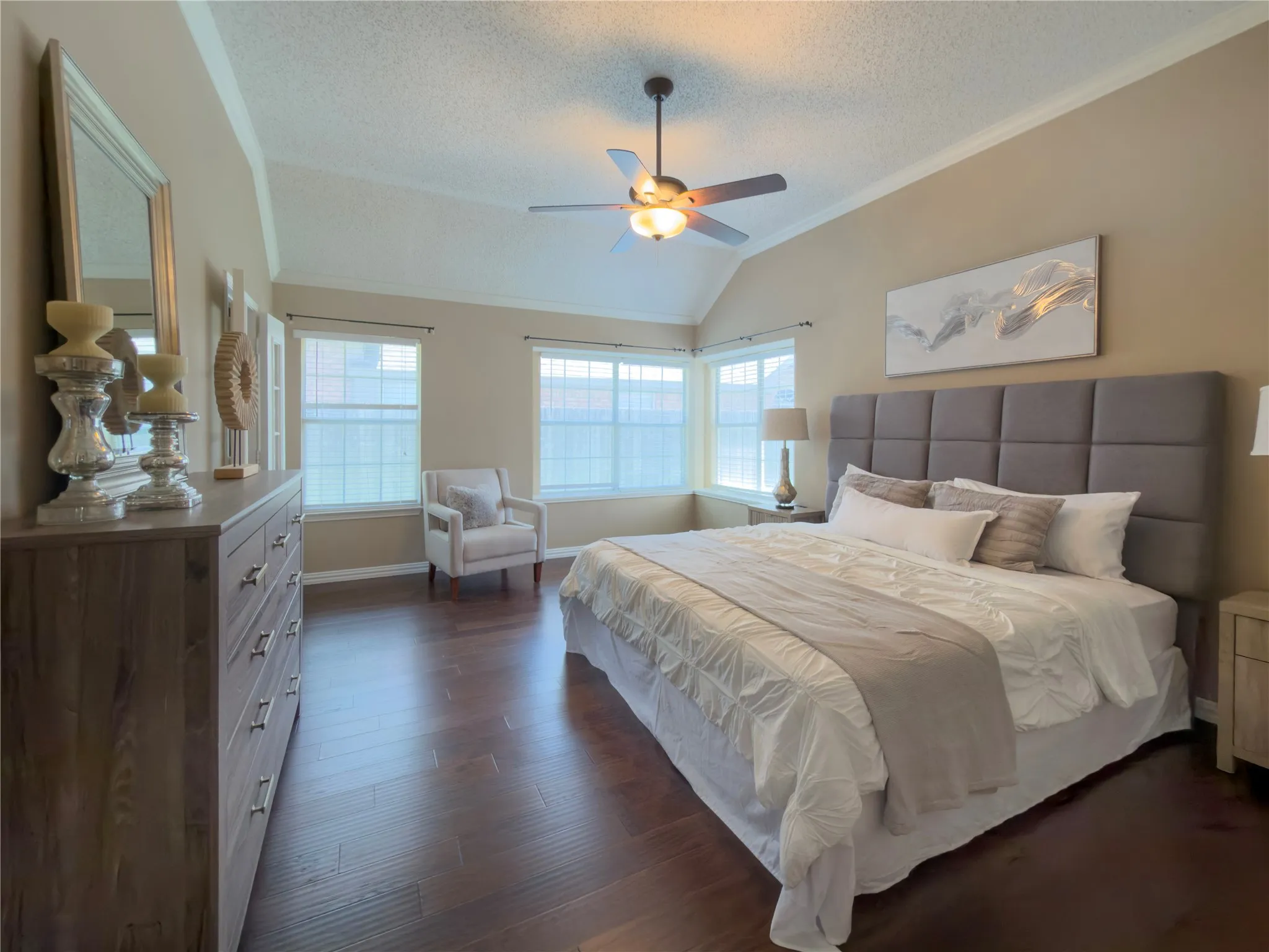Tray ceiling with crown molding, wood-finish flooring, ceiling fan with integrated lighting, multiple windows, and a built-in window seat