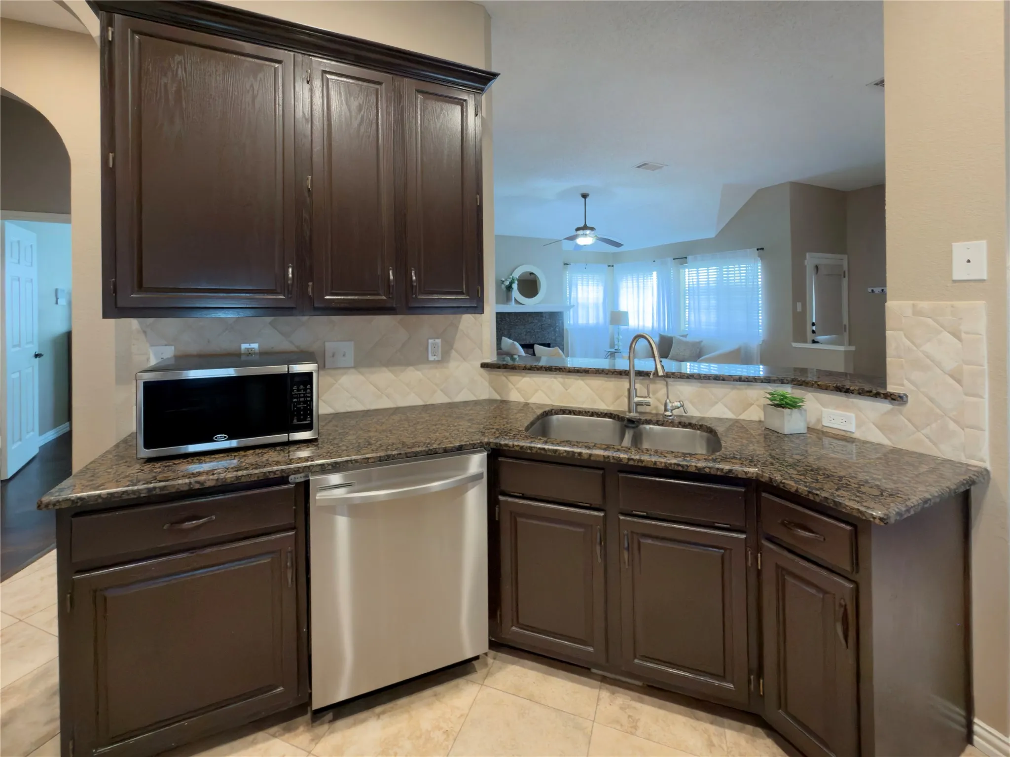 Kitchen featuring dark wood-finish cabinetry, granite countertops, a double basin stainless steel sink, and a tiled backsplash