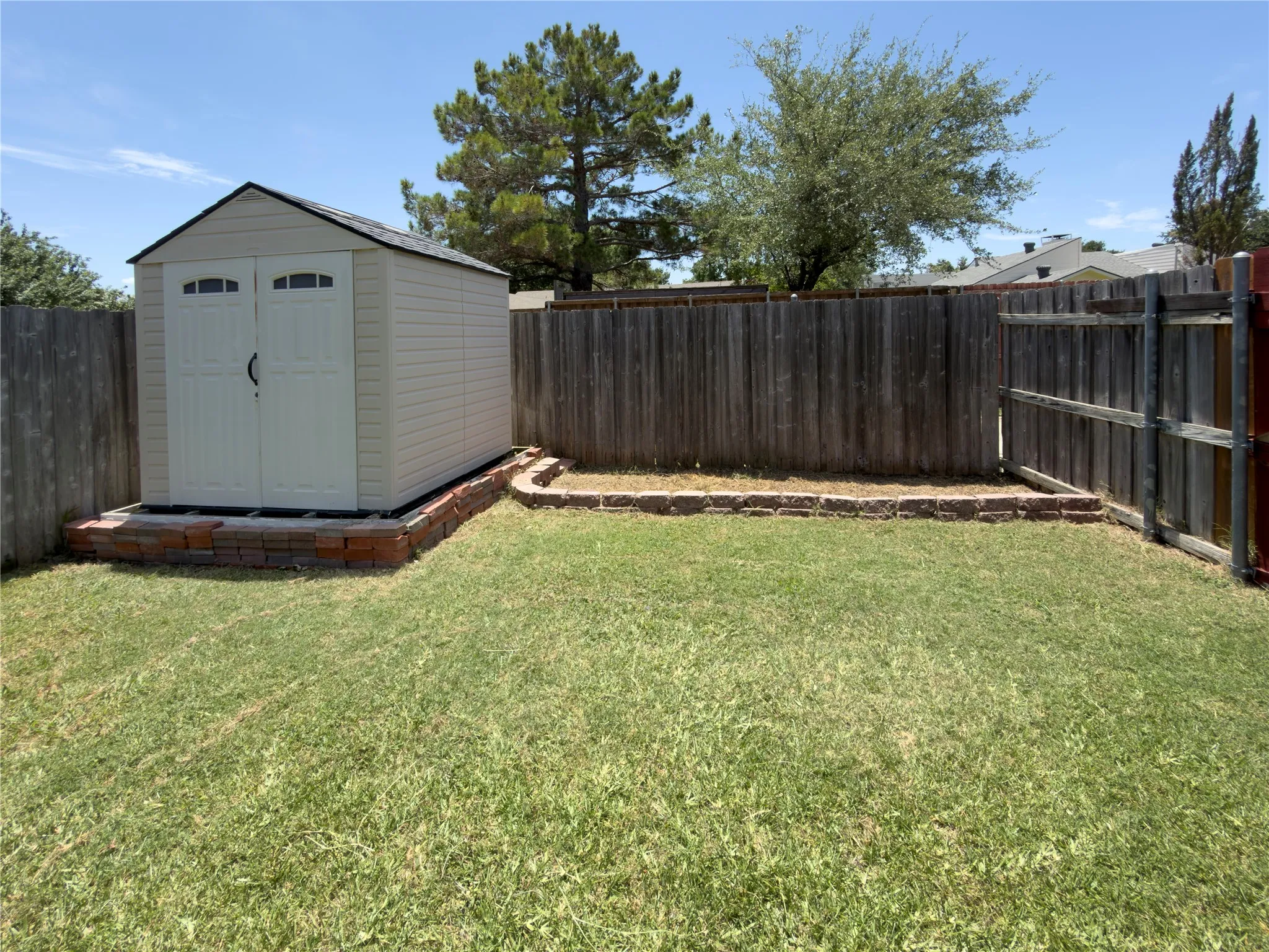 Expansive lawn featuring a utility shed with dual doors, a brick-lined perimeter, and wood fencing