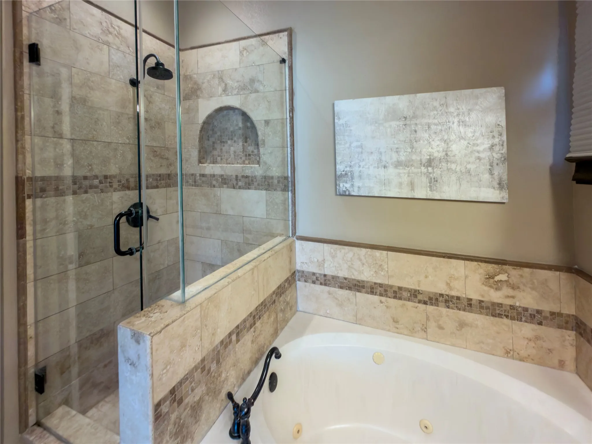 Glass-enclosed shower with a built-in niche, jetted soaking tub, and tile surround featuring a mosaic accent band