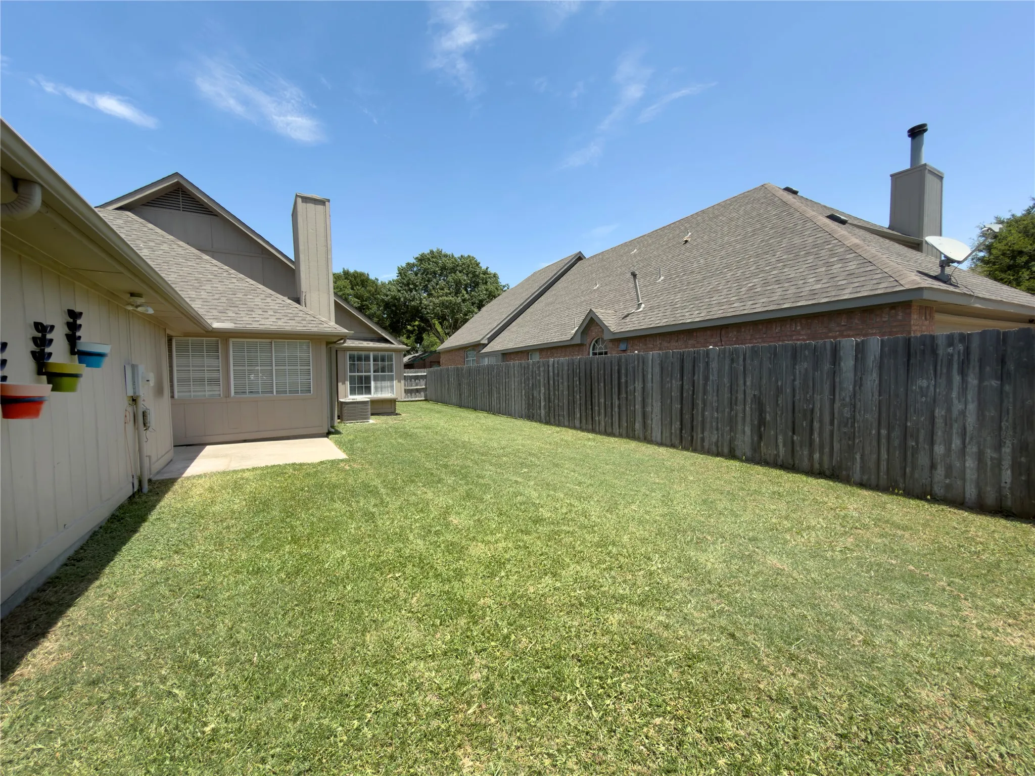 Expansive grassy yard with a concrete patio, wood privacy fence, and multiple windows