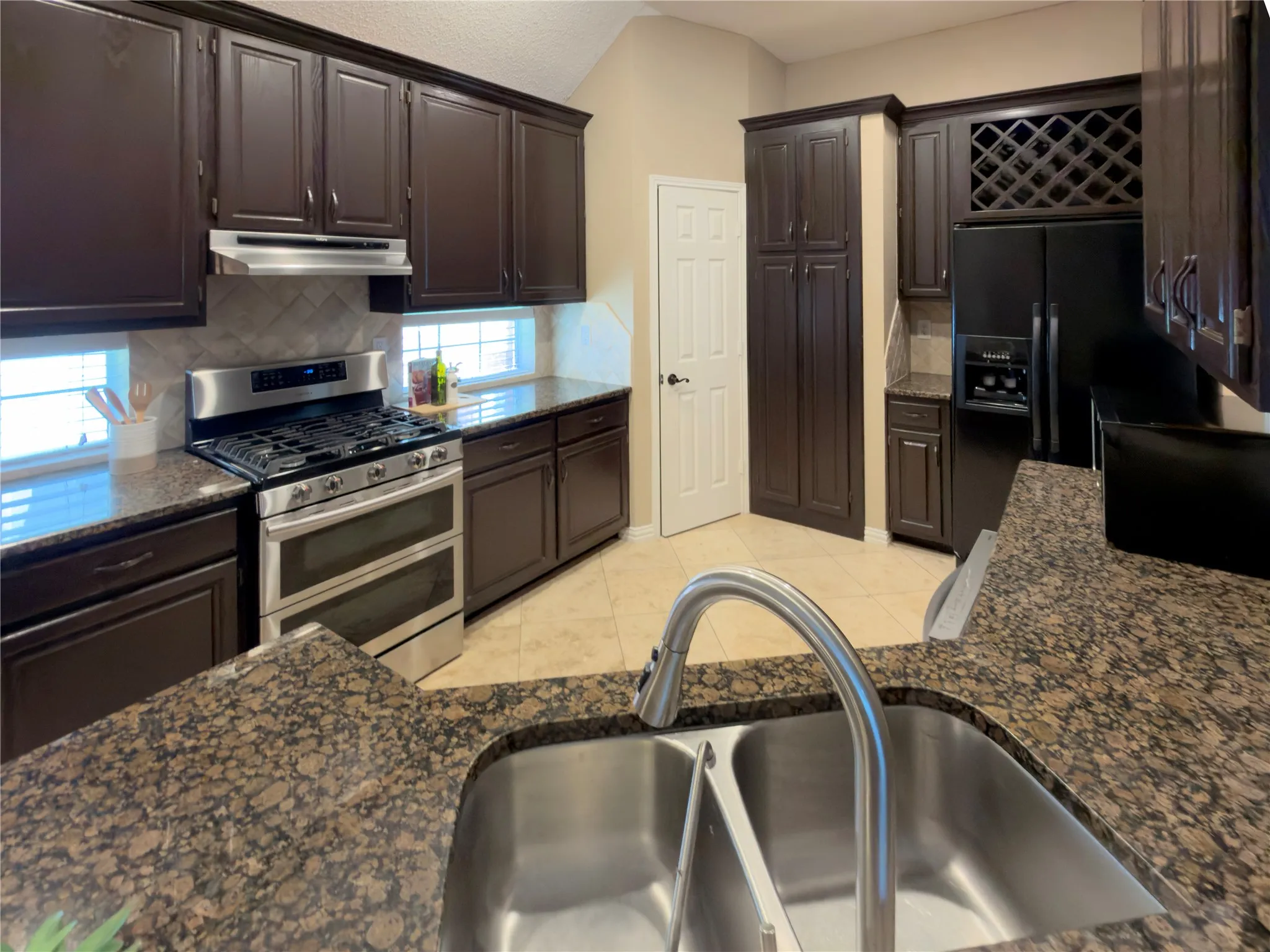 Full kitchen featuring dark wood cabinetry, stainless steel appliances, speckled stone countertops, and a dual basin sink with a gooseneck faucet