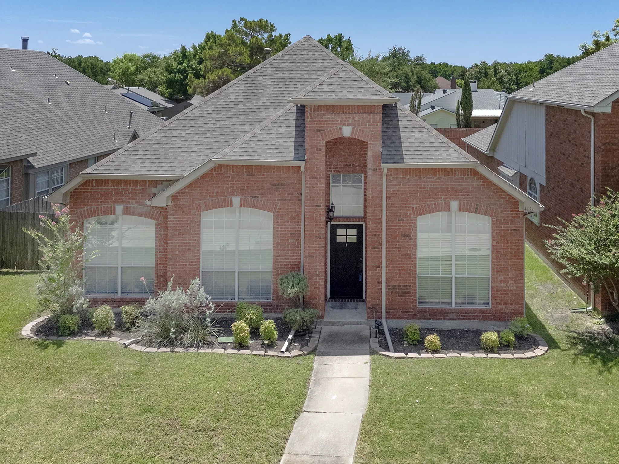 Red brick exterior with arched window details, black entry door, symmetrical front landscaping, and a pitched shingle roof