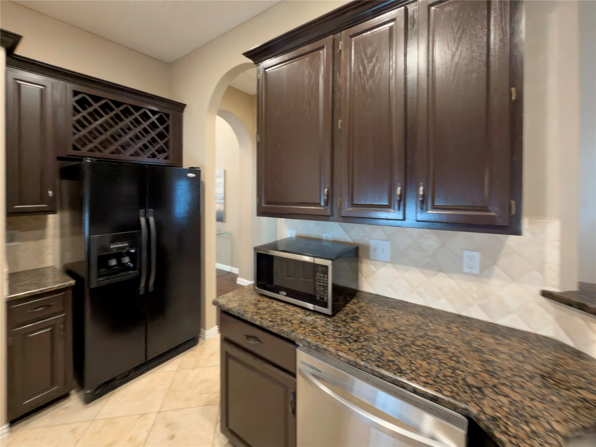 Dark wood cabinetry, built-in wine rack, tile flooring, granite countertops, and a tile backsplash