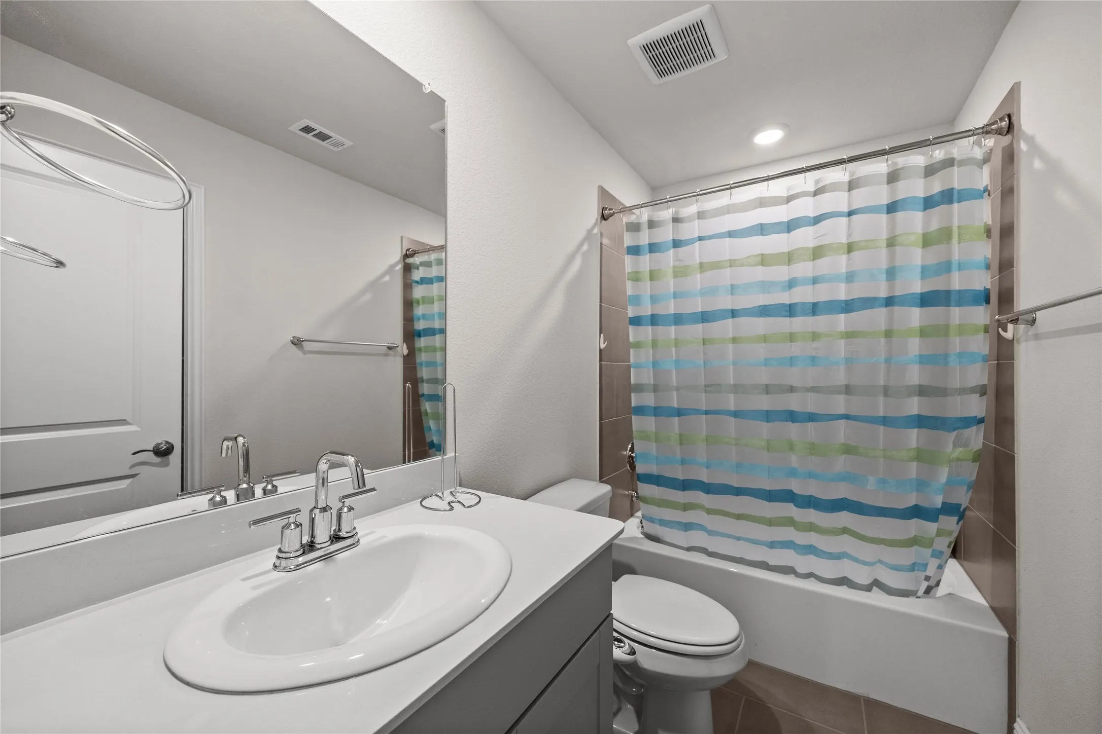 Vanity with a white oval sink and chrome faucet, large wall mirror, and a built-in bathtub with tiled surround