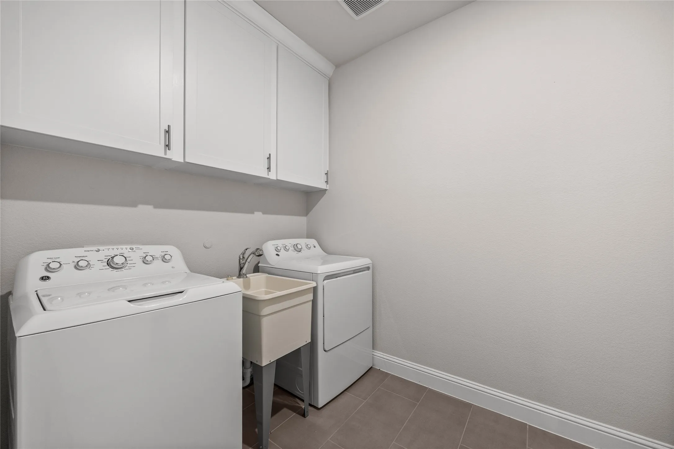 Upper cabinetry with dark hardware, utility sink with faucet, and tile flooring