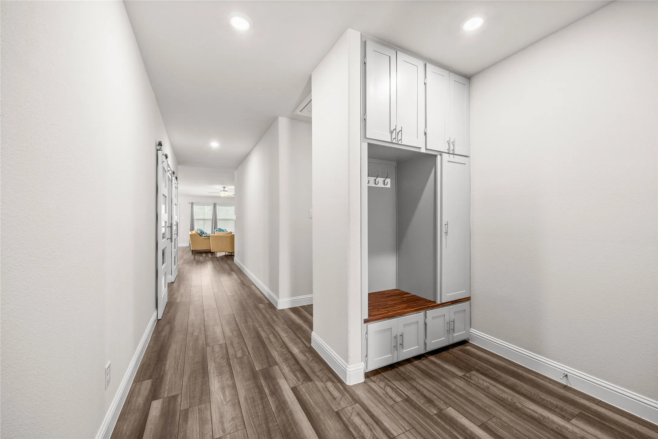 Hallway featuring wood-finish flooring, recessed lighting, and a built-in mudroom-style storage unit with cabinet doors and a wood bench