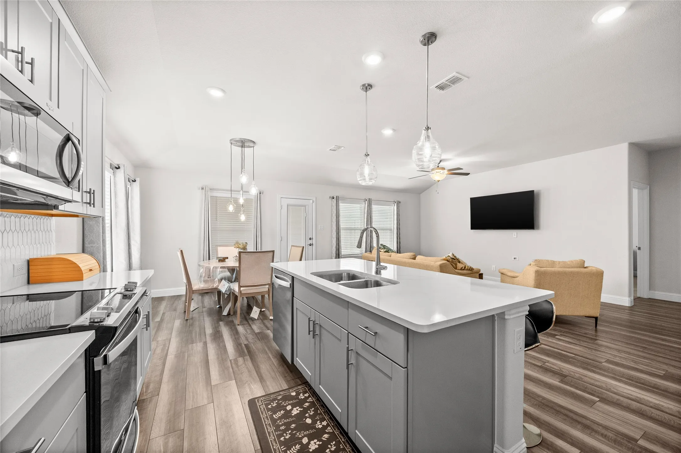 Kitchen featuring gray cabinetry, a central island with dual sinks, and pendant lighting