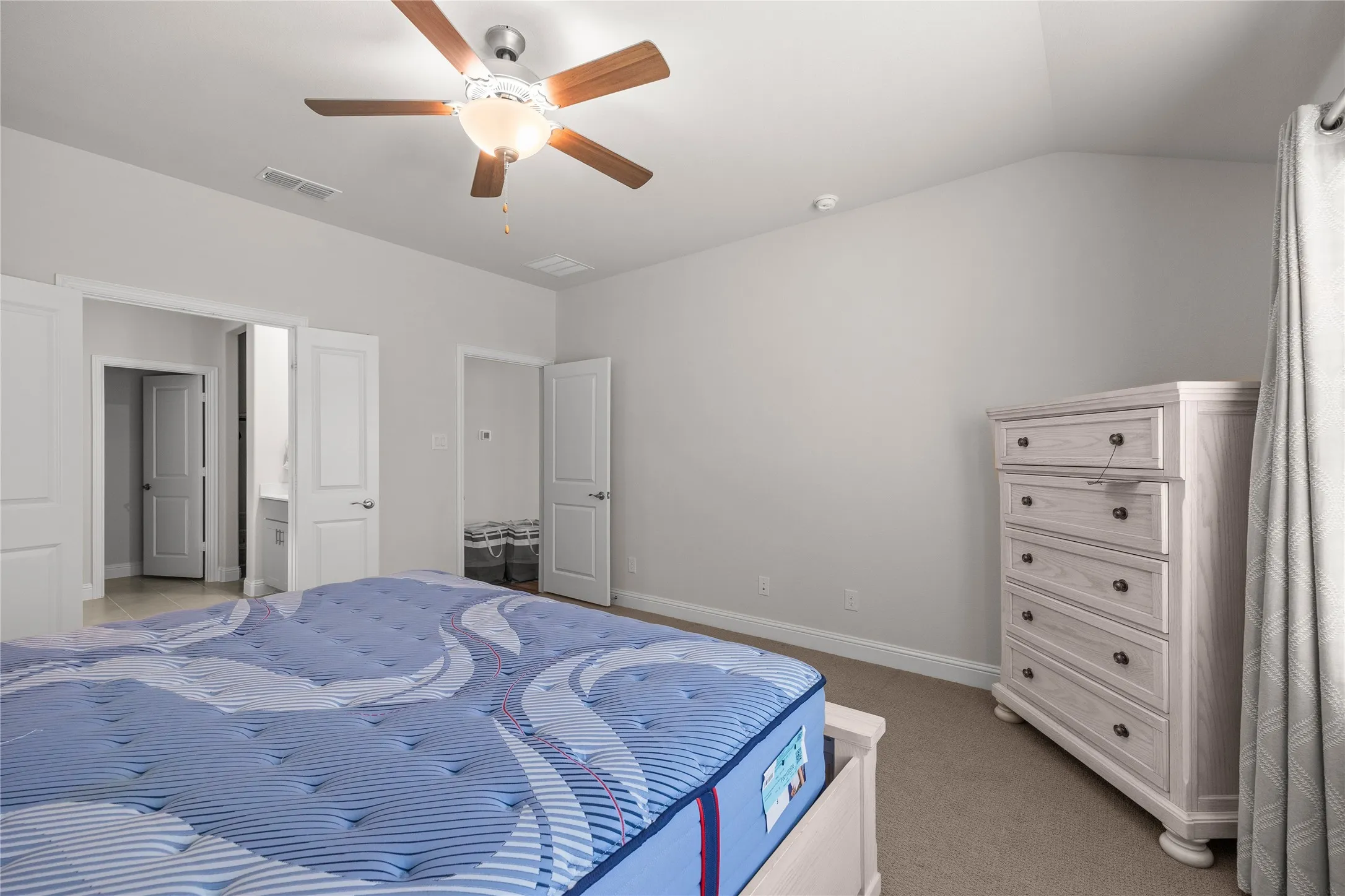 Vaulted ceiling with a wood-finish ceiling fan, neutral wall paint, and beige carpeting
