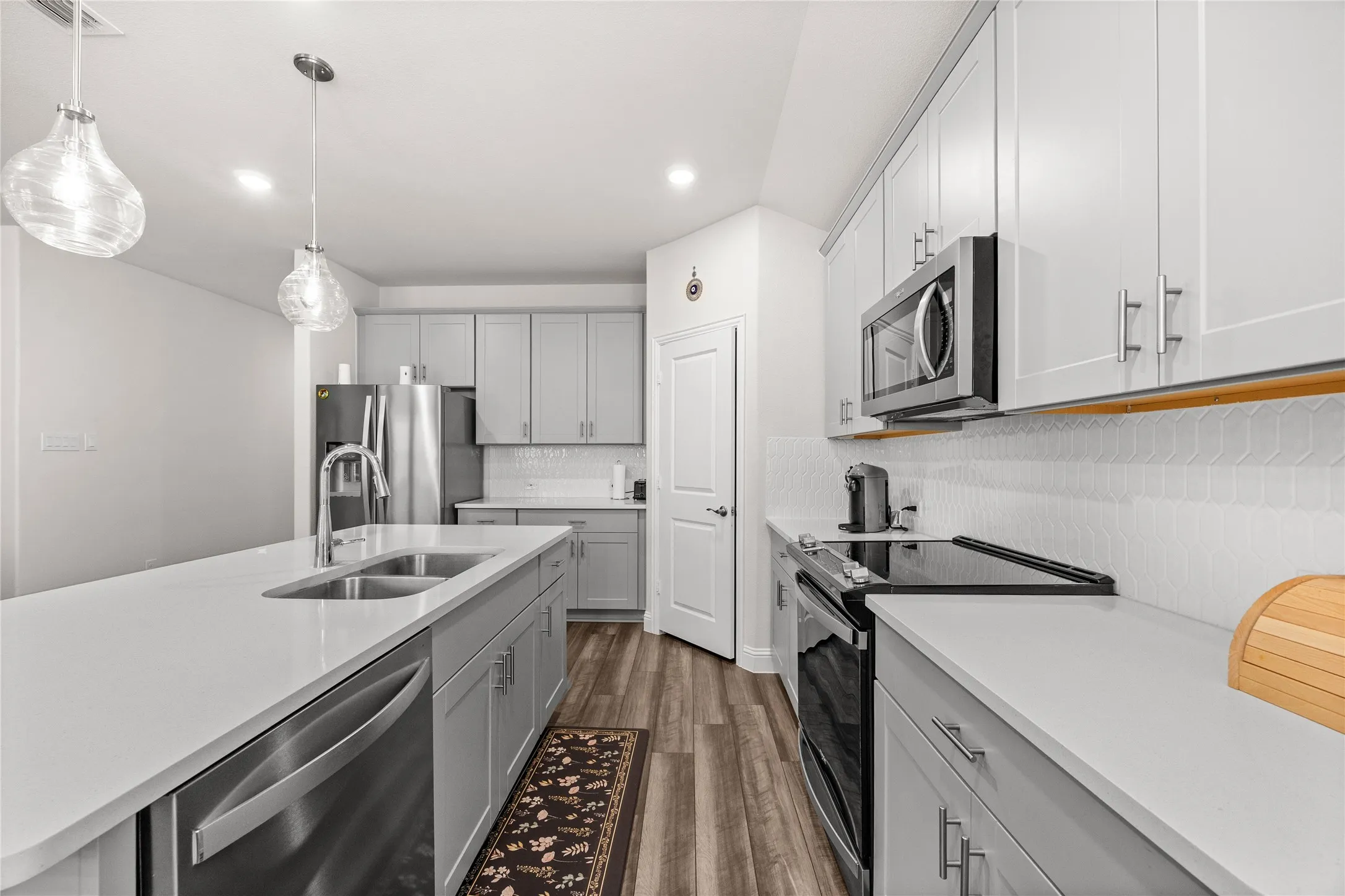 Kitchen featuring an island with a dual-basin stainless steel sink, stainless steel appliances, light gray cabinetry, white countertops, and wood-finish flooring