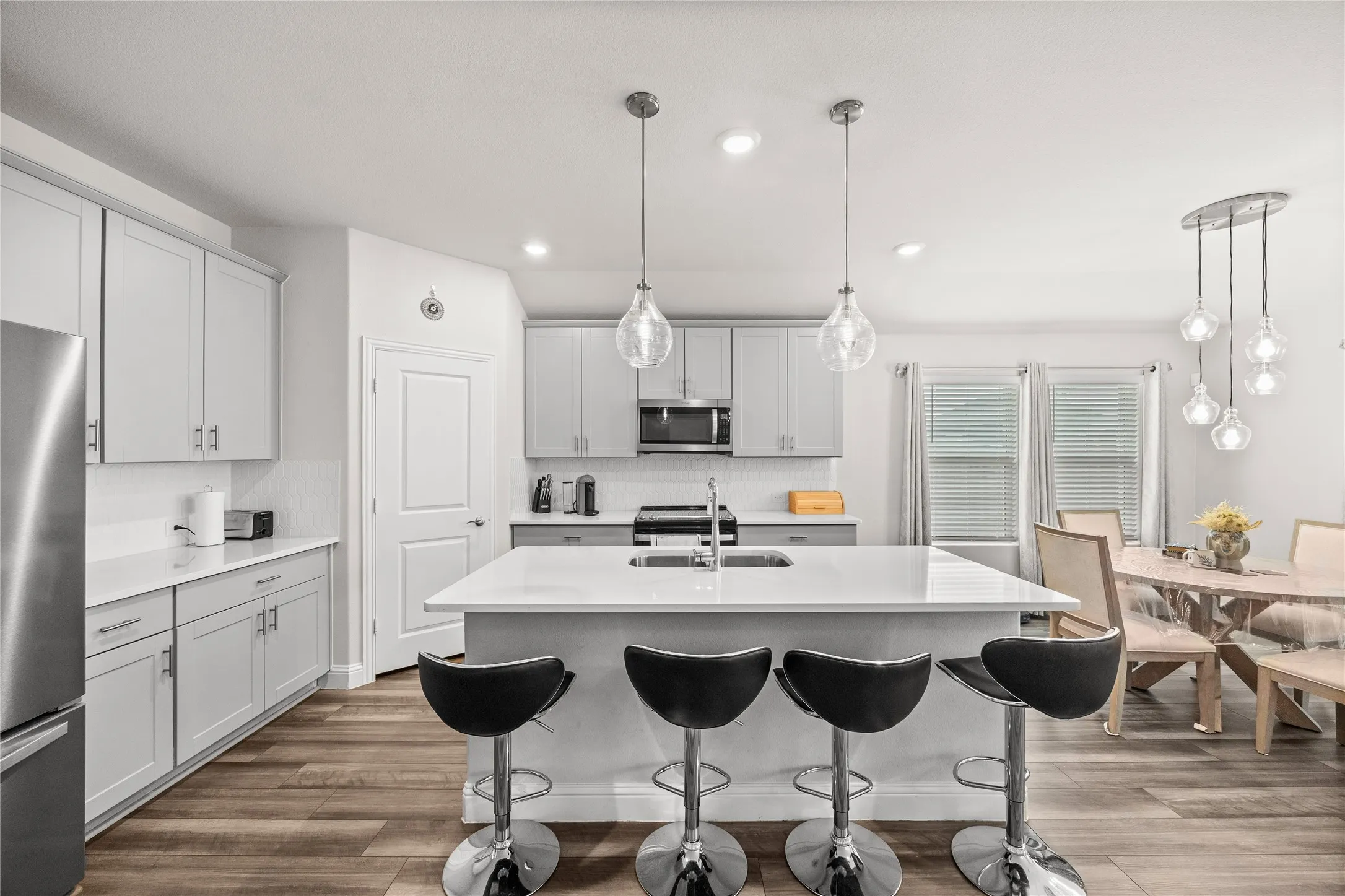Modern kitchen featuring light gray cabinetry, stainless steel appliances, a center island with sink, and wood-finish flooring