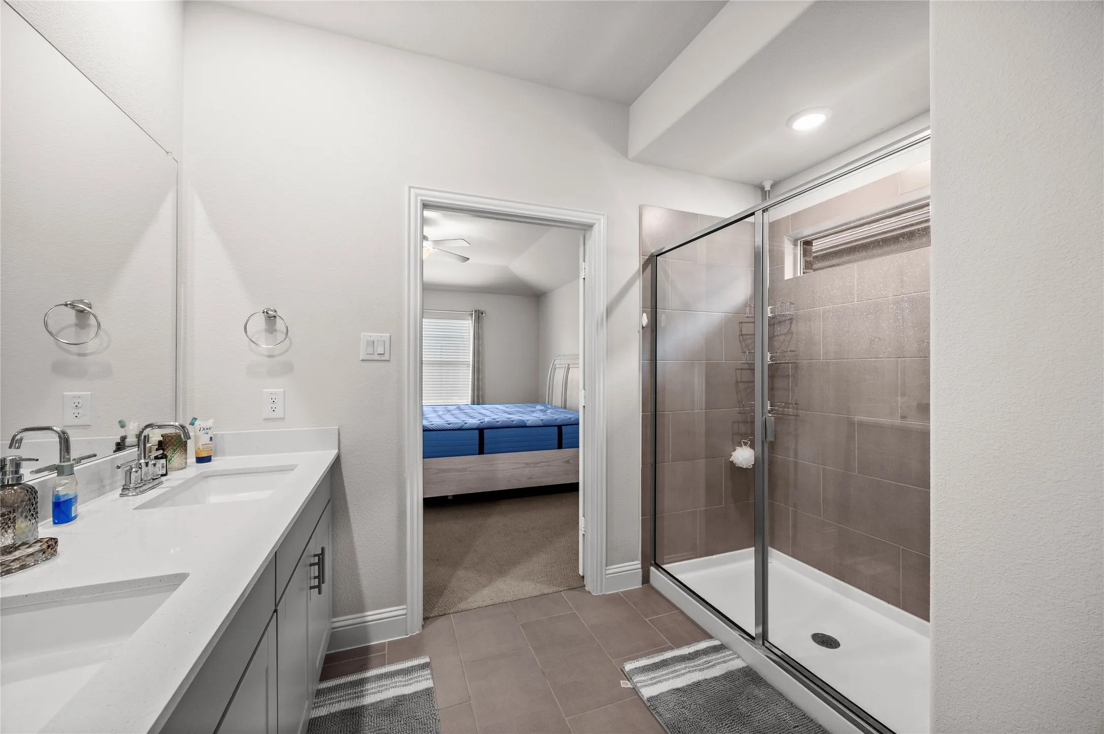 Dual vanity with undermount sinks and chrome fixtures, frameless glass shower enclosure, tiled shower surround, recessed lighting, and tile flooring