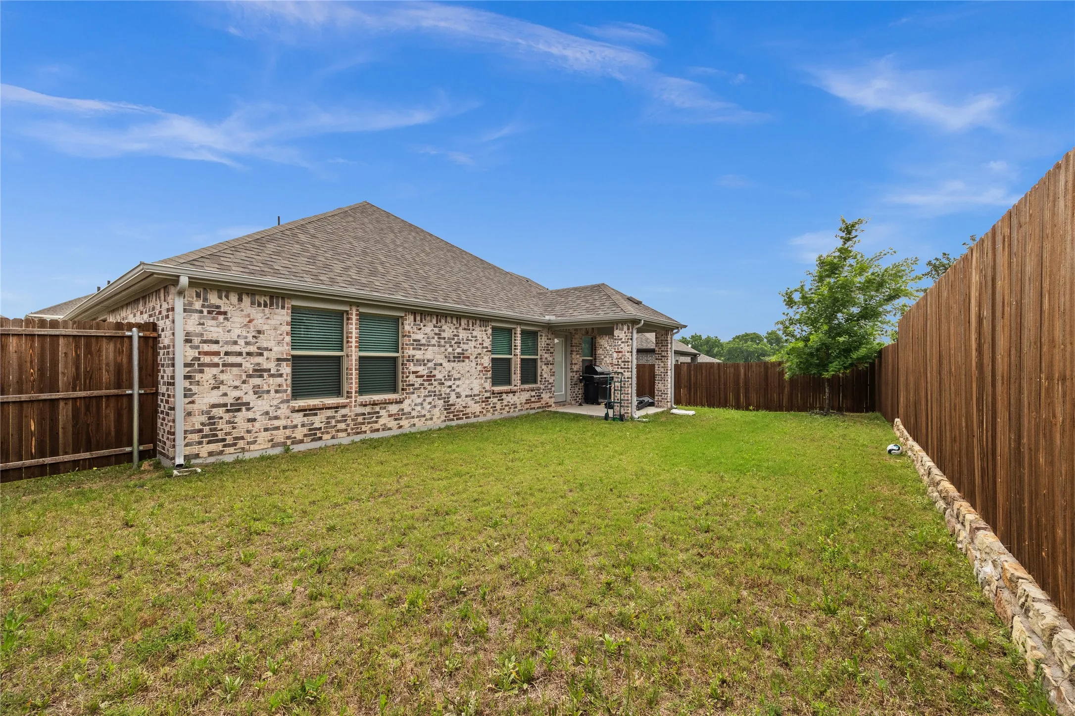Expansive fenced backyard featuring a stone-lined perimeter