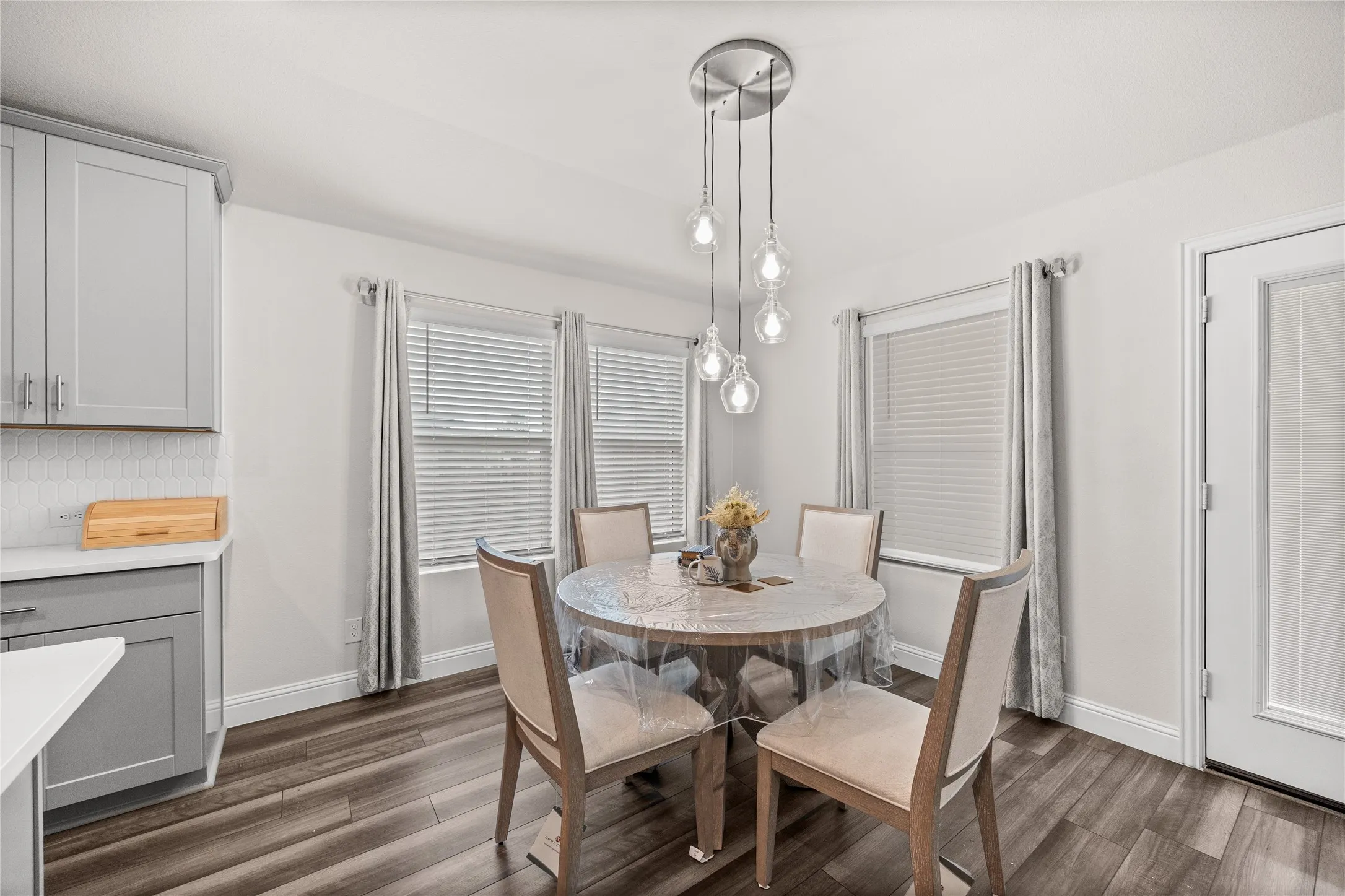 Wood-finish flooring with white baseboards, a multi-bulb pendant light fixture, and white walls