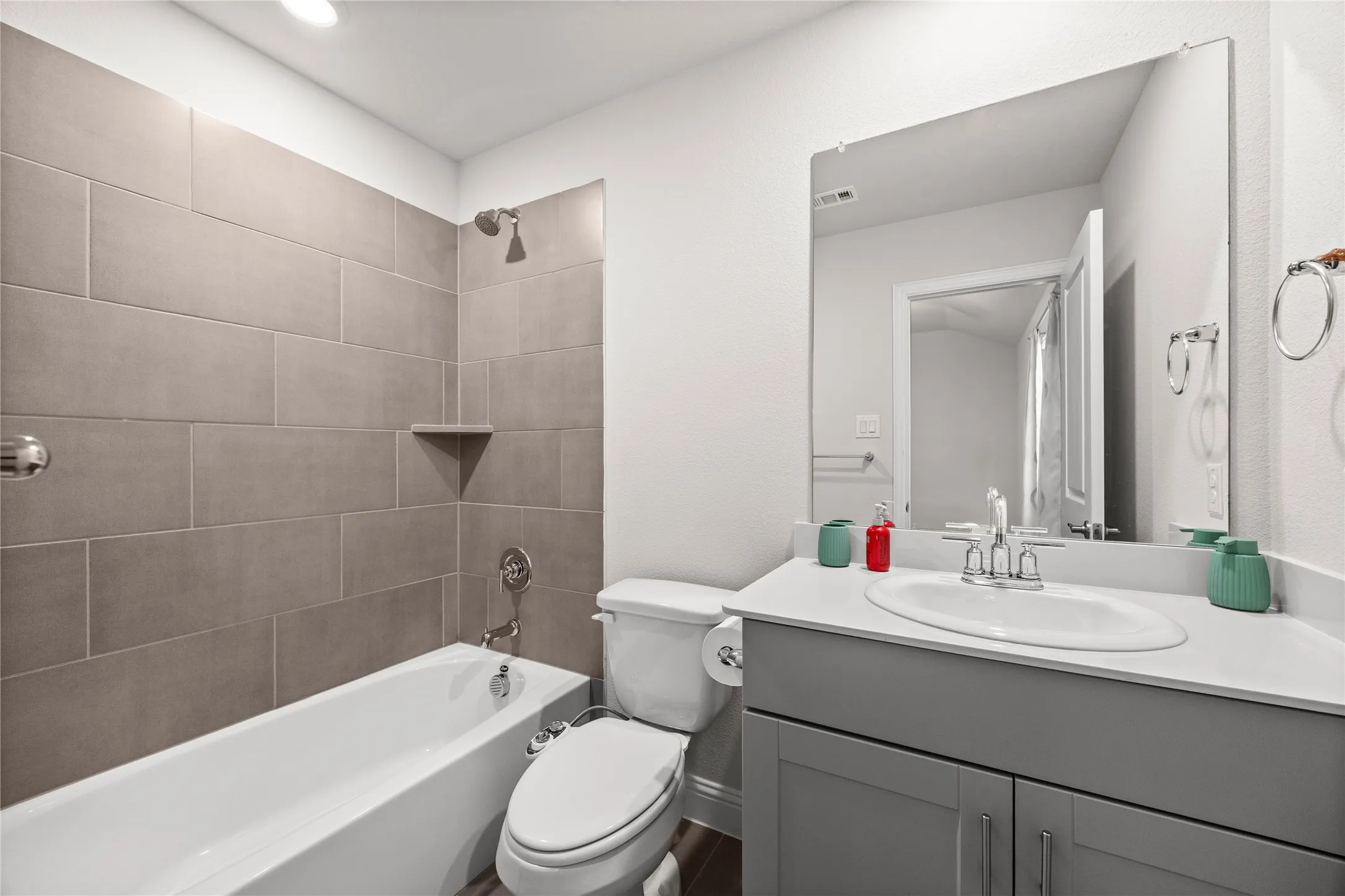 White tub with gray tiled surround, integrated shower niche, and brushed nickel fixtures