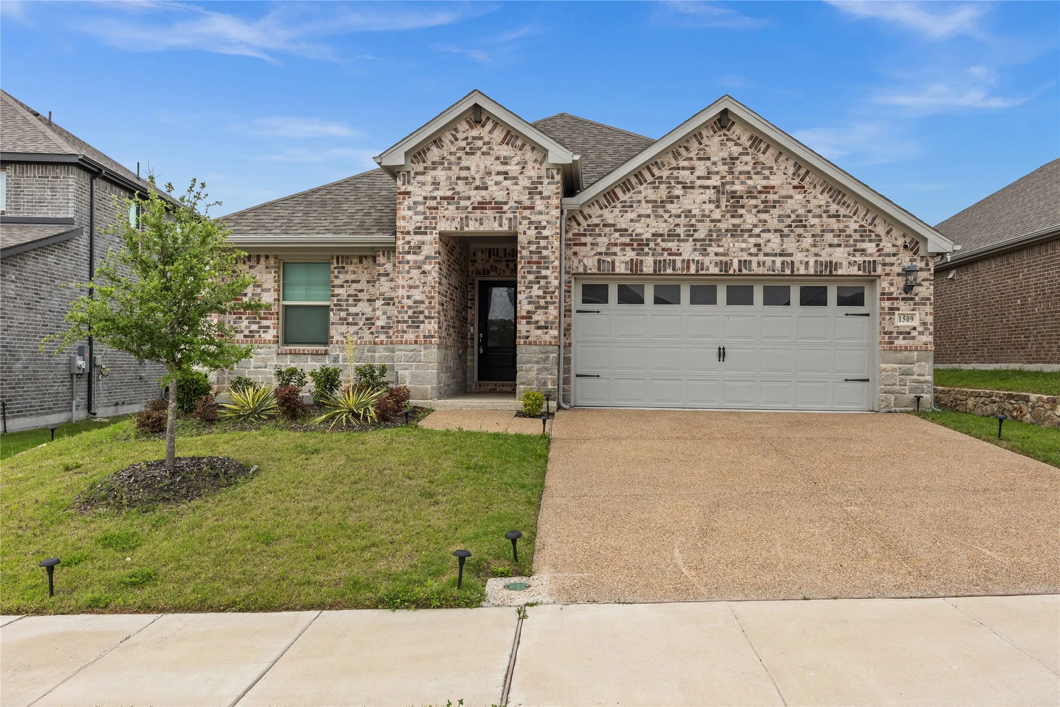 Brick and stone facade with an attached garage, a paved driveway, and a landscaped front yard