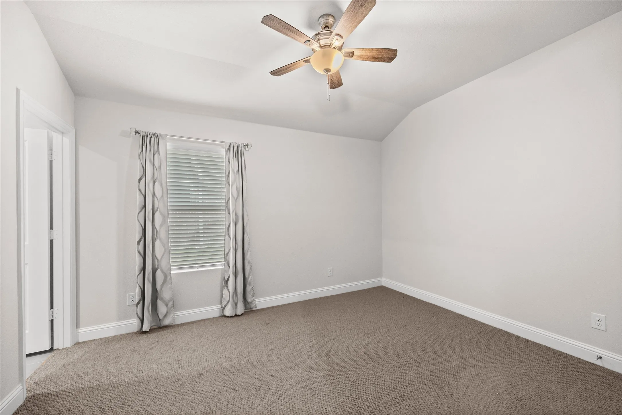 Neutral wall color, vaulted ceiling, ceiling fan with light fixture, window with blinds, and carpeted flooring