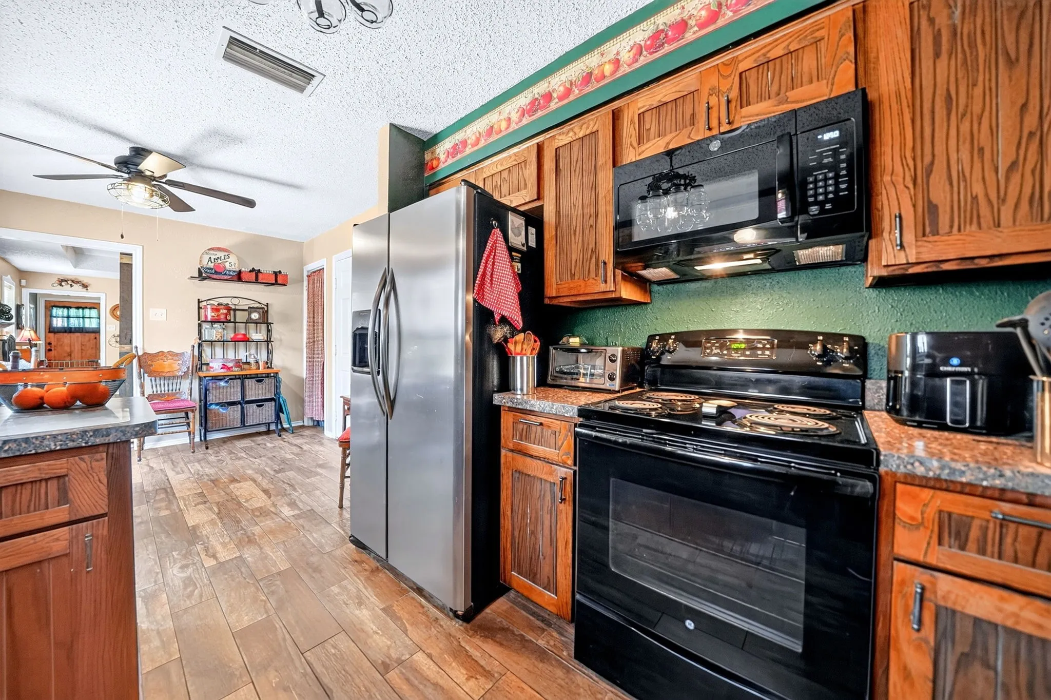 Kitchen featuring wood-finish flooring, wood cabinetry, granite-style countertops, stainless steel refrigerator, and a black electric range with an overhead microwave