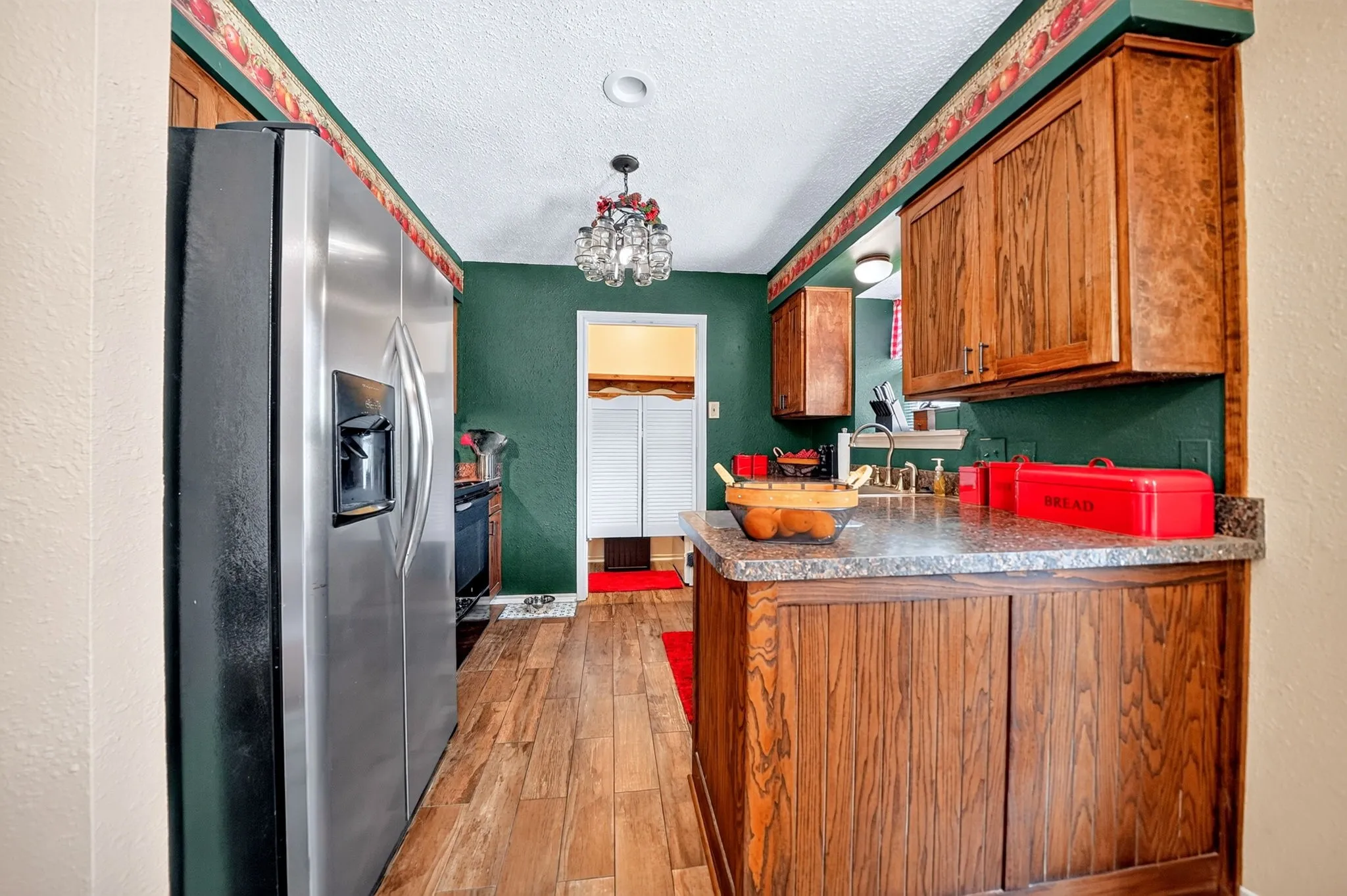 Wood-finish flooring, stainless steel refrigerator, wood cabinetry, stone-look countertops, and recessed lighting