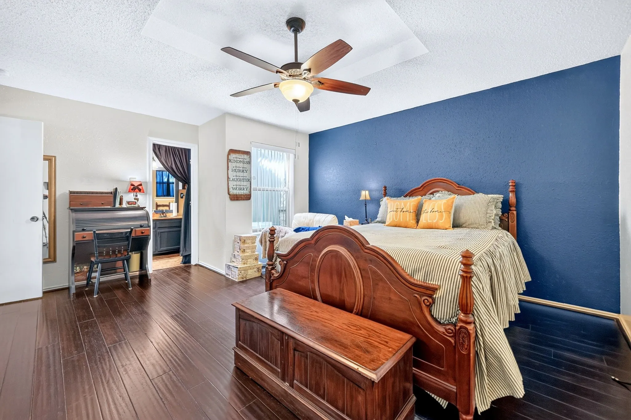 Dark wood-finish flooring with a contrasting accent wall, recessed ceiling detail, and a ceiling fan with integrated lighting