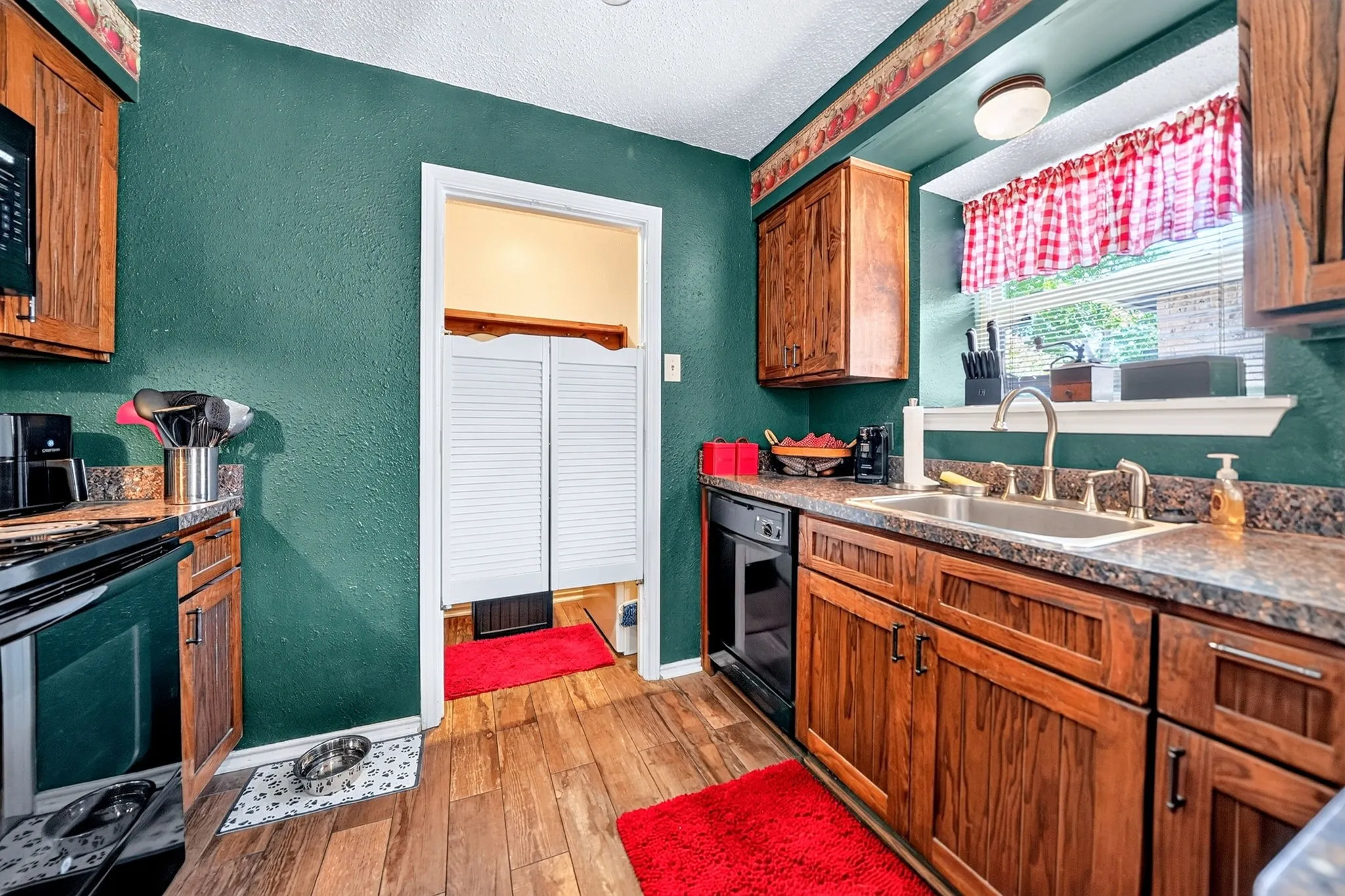 Kitchen featuring wood-finish flooring, wood cabinetry, stone-finish countertops, a double basin sink with a gooseneck faucet, and a built-in dishwasher
