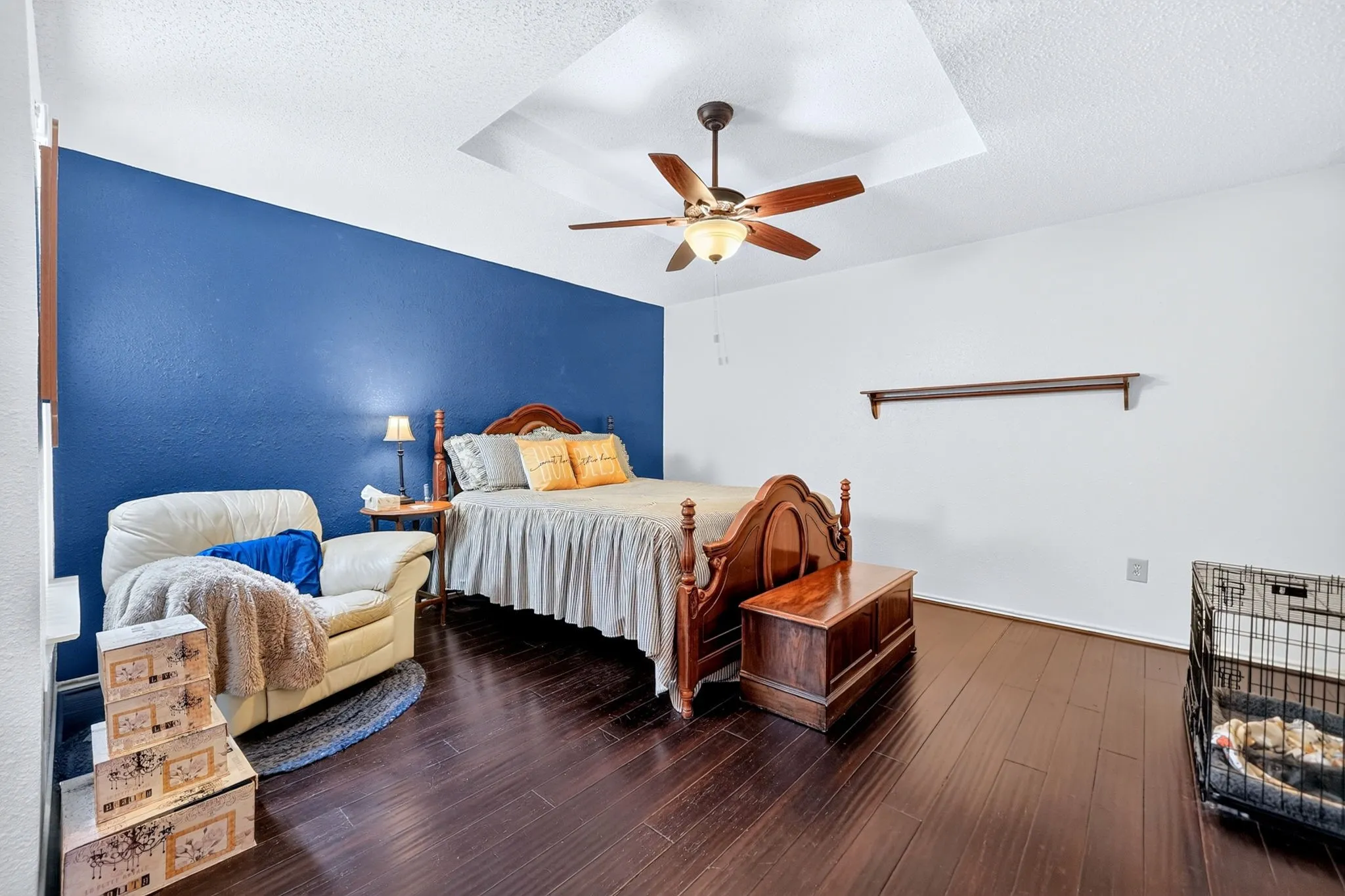 Tray ceiling with a ceiling fan, dark wood-finish flooring, and a decorative wall shelf