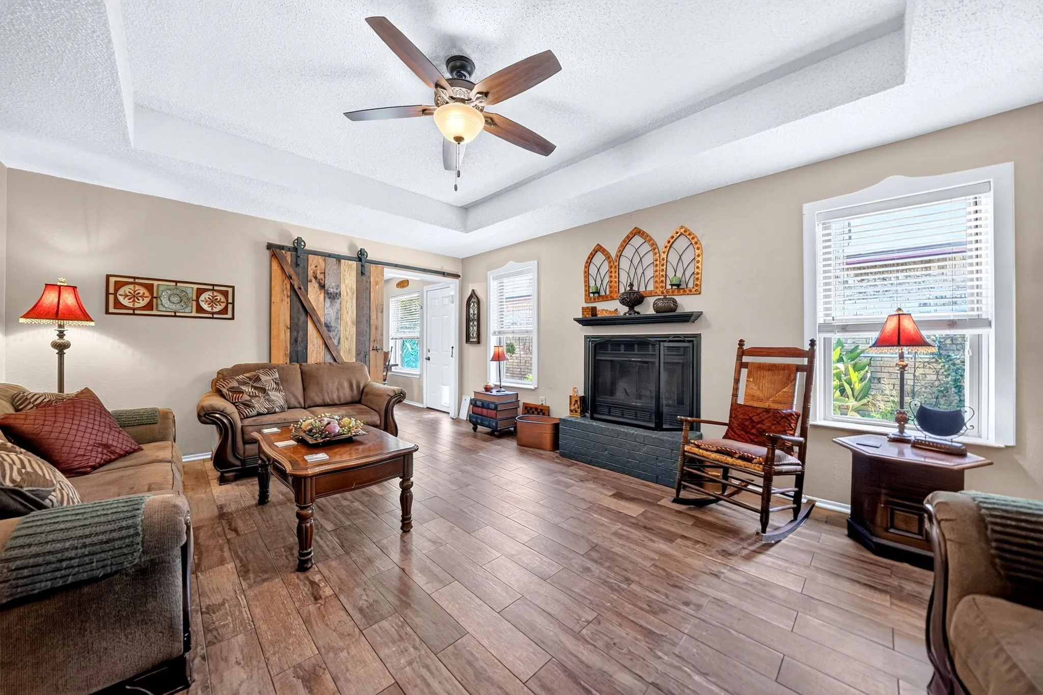 Tray ceiling with a ceiling fan, wood-finish flooring, fireplace with a black mantel, and a barn door entry