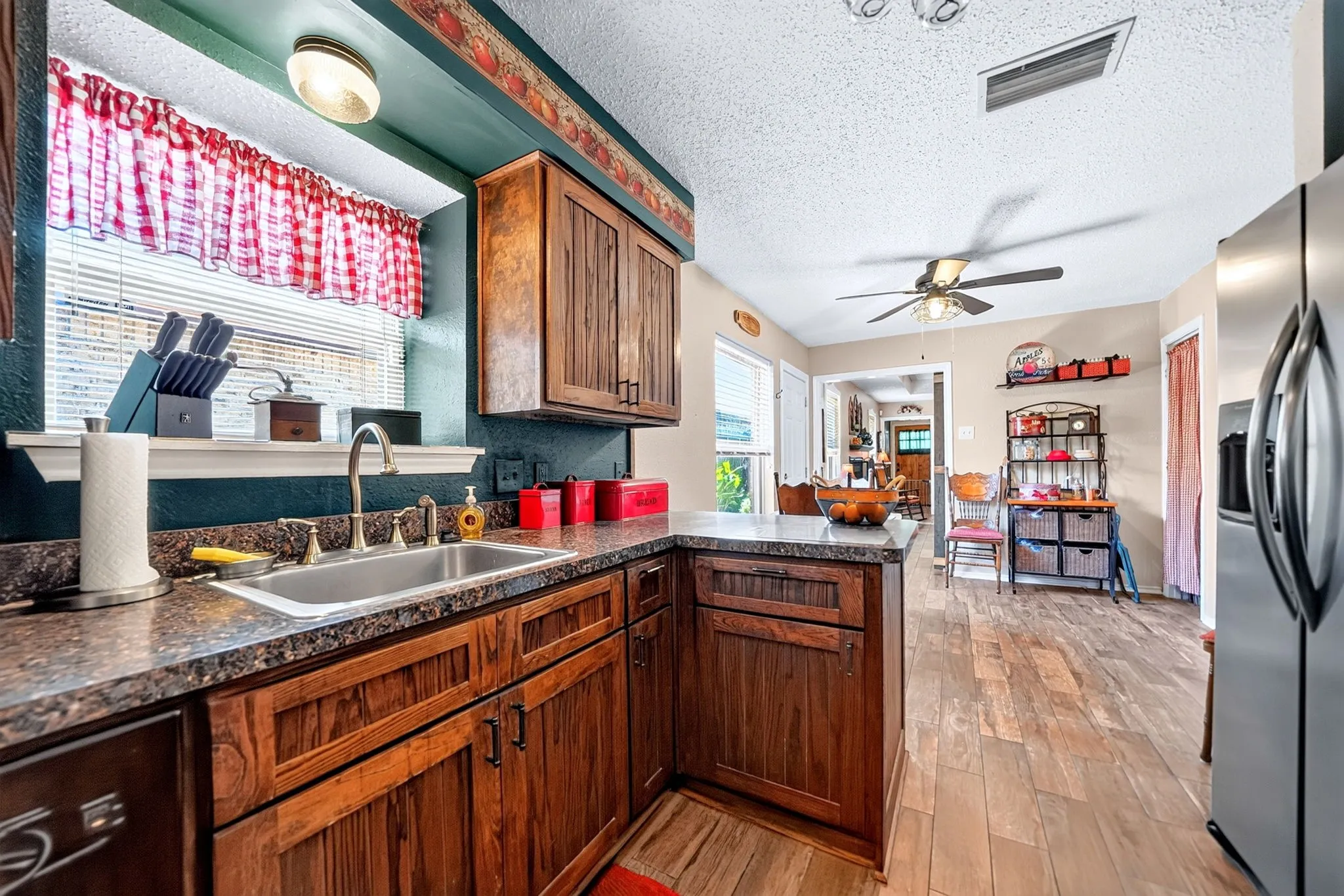 Kitchen featuring wood-finish cabinetry, a stainless steel sink with a high-arc faucet, stone-look countertops, and wood-finish flooring