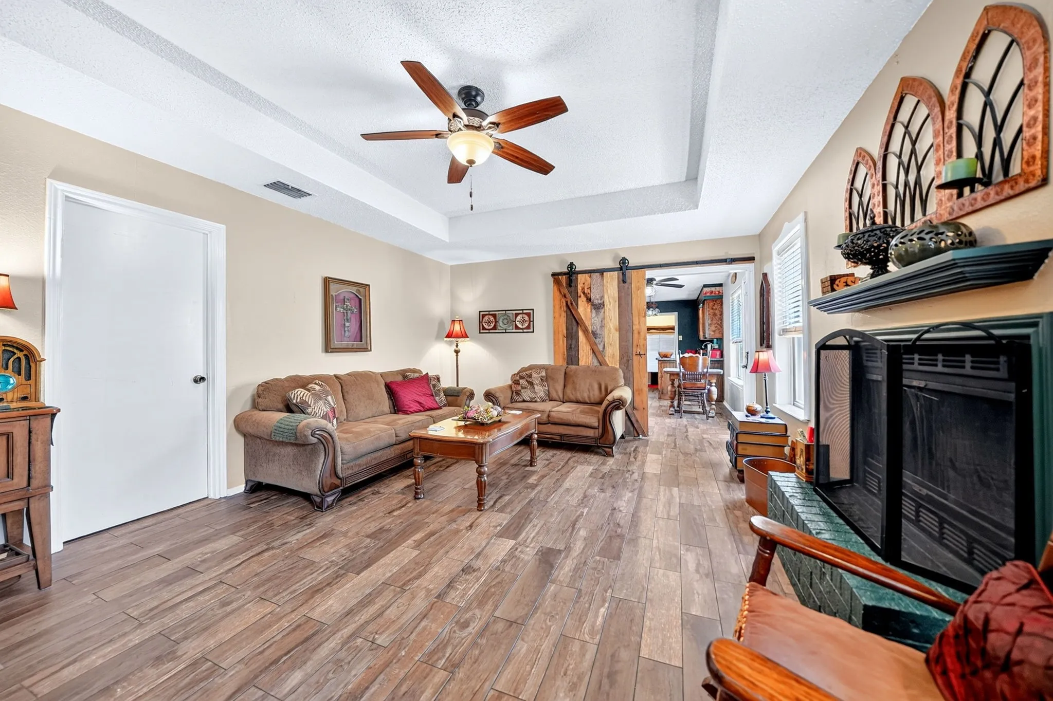 Tray ceiling with a ceiling fan, wood-finish flooring, and a fireplace with a black screen