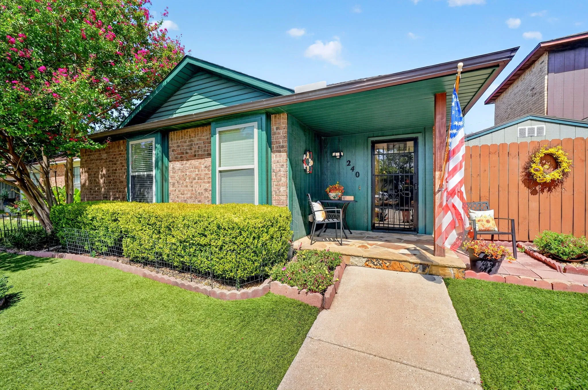 Brick exterior with teal siding and trim, featuring a covered front porch, concrete pathway, and mature landscaping