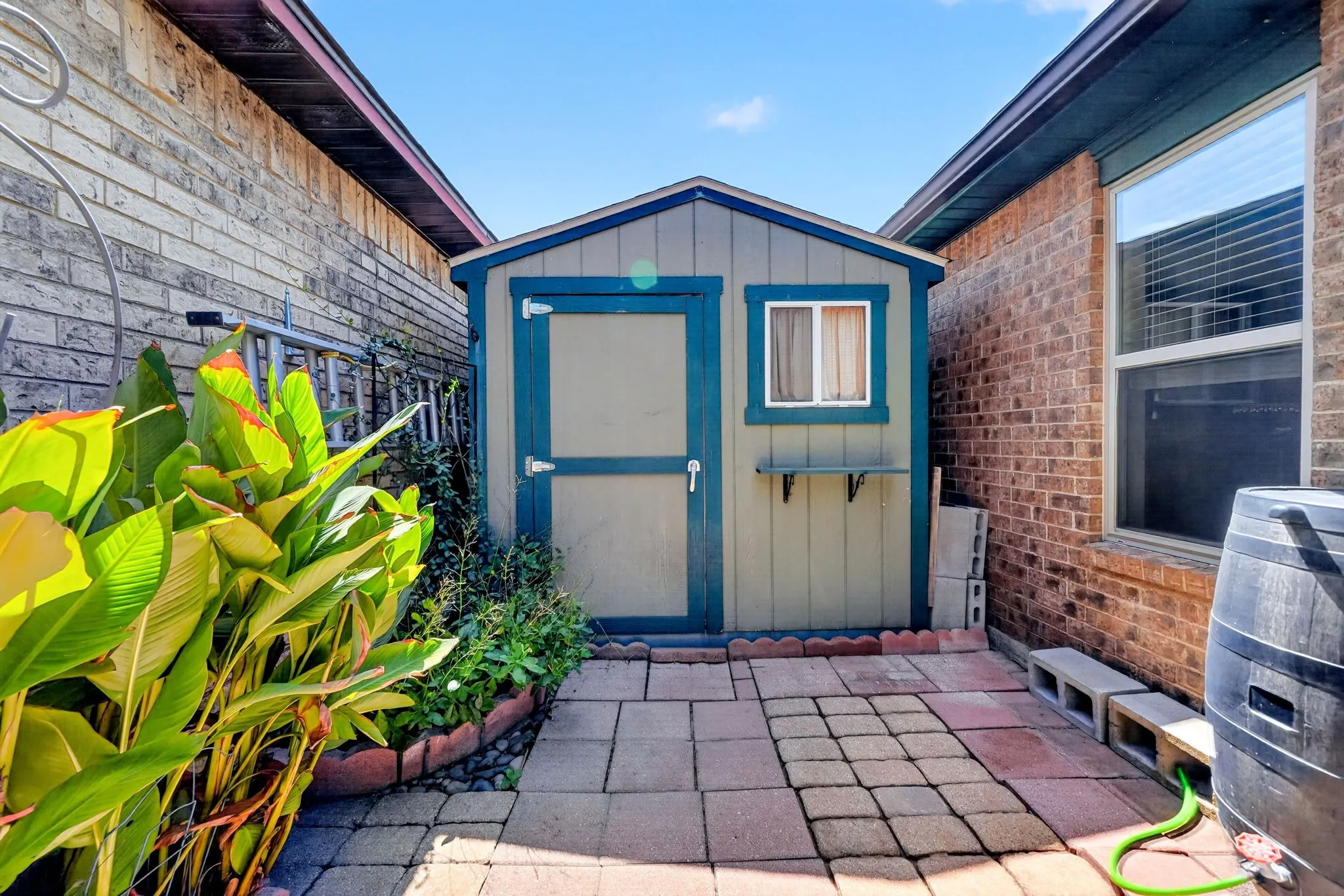 Paved patio area with a storage shed featuring a window, and brick exterior construction