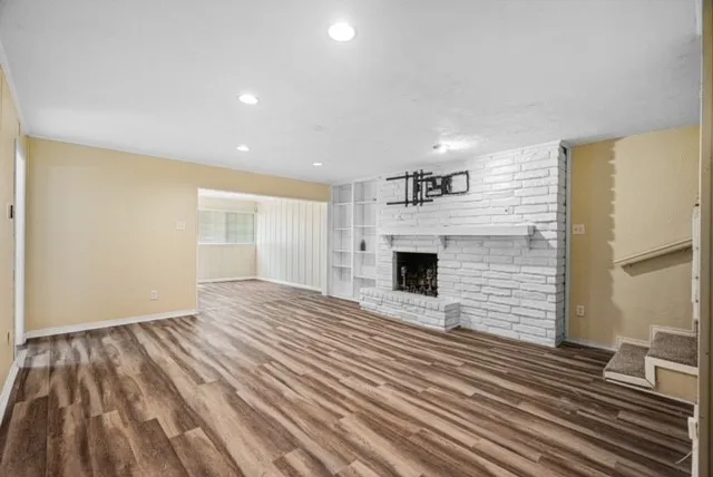 Spacious interior featuring wood-finish flooring, a white brick fireplace with mantel, recessed lighting, and built-in shelving