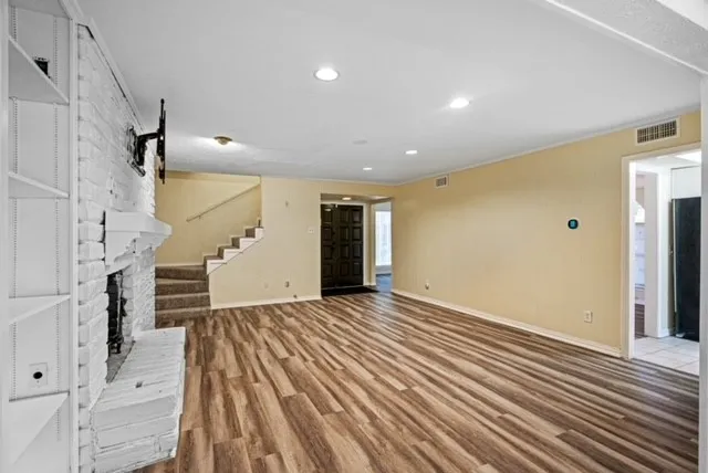 Wood-finish flooring, recessed lighting, and a white-painted brick fireplace with built-in shelving