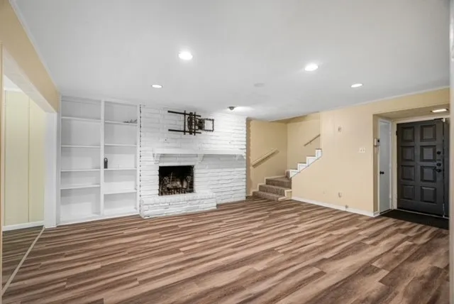Wood-finish flooring, white brick fireplace, recessed lighting, built-in shelving, and a paneled entry door