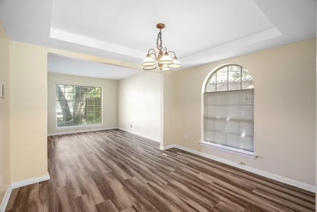 Tray ceiling with a decorative chandelier, wood-finish flooring, and an arched window