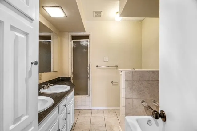 Double vanity with under-mount sinks, dark stone-finish countertop, white cabinetry, and a shower enclosure with a frosted door