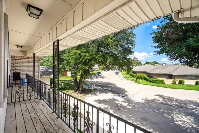 Upper-level balcony with wood-finish flooring, wrought iron railing, and overhead lighting