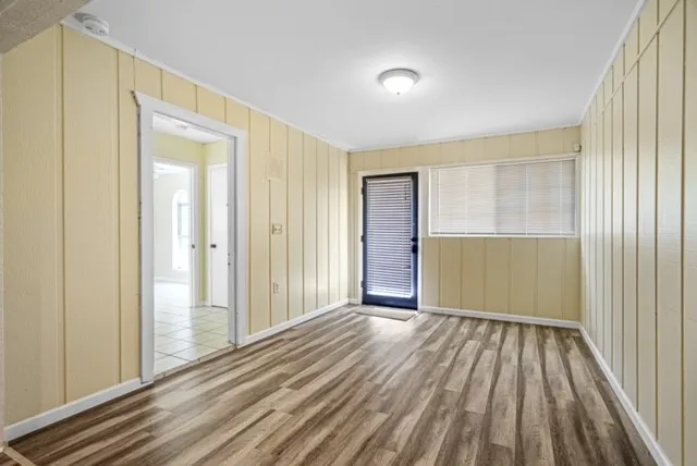 Wood-finish flooring, vertical paneling, recessed lighting, and an exterior door with integrated blinds