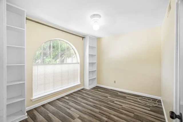 Arched window with privacy blinds, wood-finish flooring, recessed ceiling light fixture, and built-in shelving on opposing​​‌​​​​‌​​‌‌​‌‌​​​‌‌​‌​‌​‌​​​‌​​ walls