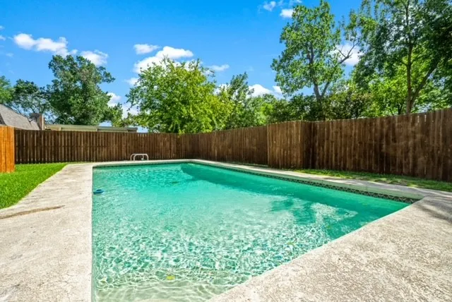In-ground swimming pool with a concrete surround, wood privacy fencing, and surrounding green lawn