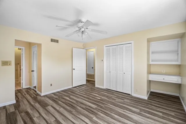 Wood-finish flooring, built-in shelving, built-in desk, louvered bi-fold closet doors, and ceiling fan
