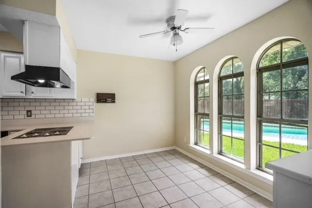 Kitchenette featuring a tile backsplash, cooktop, white cabinetry, and an exhaust hood