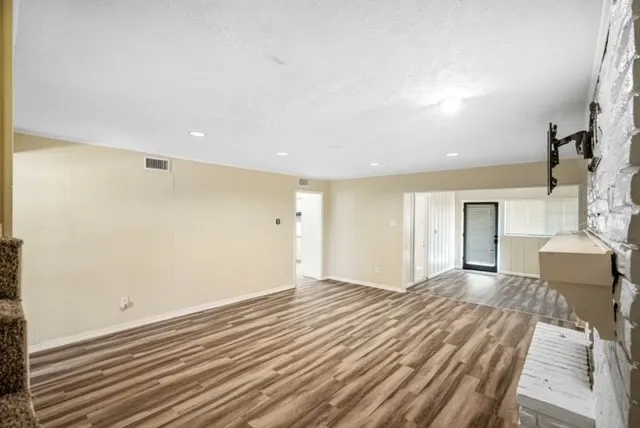 Spacious living area featuring wood-finish flooring, a white painted brick fireplace, and recessed lighting