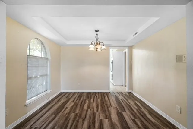 Tray ceiling with a chandelier, wood-finish flooring, and an arched window